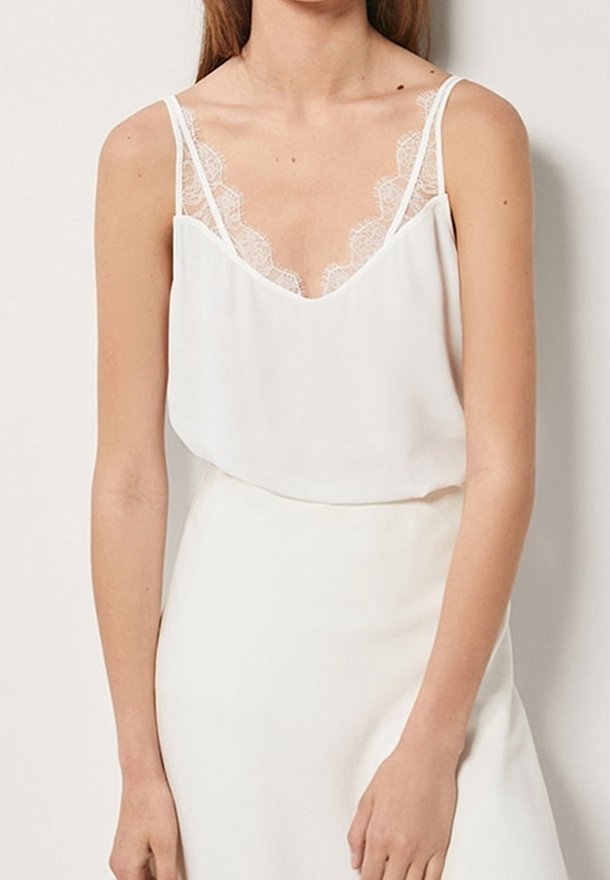 Canotte bianca con rifiniture in pizzo lungo il décolleté e le bretelle, con vestibilità ampia e texture morbida. Progettata con un décolleté a forma di V.