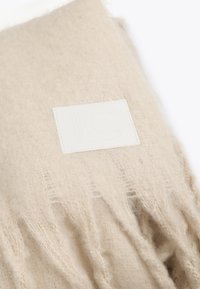 Biserna vunena šal s mekim, teksturiranim završetkom, sa detaljima resica i pravokutnom bijelom etiketom s utisnutim logotipom.