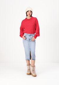 Röd överdimensionerad stickad tröja, ljusblå denimkjol med slits fram, beige pälsfodrade stövlar, gräddfärgad stickad mössa.
