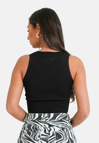 Czarny prążkowany top bez rękawów o okrągłym dekolcie. Materiał jest teksturowany, dopasowany i zestawiony z wzorzystymi spodniami o wysokim stanie.