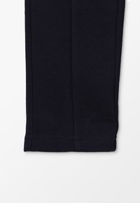 Pantalon bleu marine en tissu texturé, avec une coupe droite et un ourlet propre. Aucun détail ou motif supplémentaire visible.
