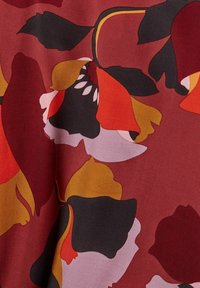 Motif floral audacieux avec de grandes pétales abstraites en noir, rouge, jaune moutarde et rose sur un fond de tissu rouge profond.