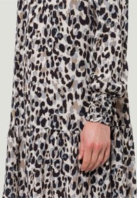 Gros plan d'une main reposant près d'un poignet froncé sur une robe à manches longues avec un motif léopard beige, noir, gris et marron.