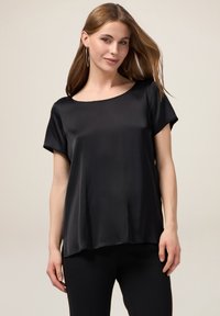 Top corto in satin nero a maniche corte con scollatura ampia e vestibilità morbida. Il tessuto ha una texture liscia, che si drappeggia delicatamente sul corpo.