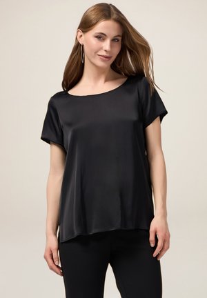 Top corto in satin nero a maniche corte con scollatura ampia e vestibilità morbida. Il tessuto ha una texture liscia, che si drappeggia delicatamente sul corpo.
