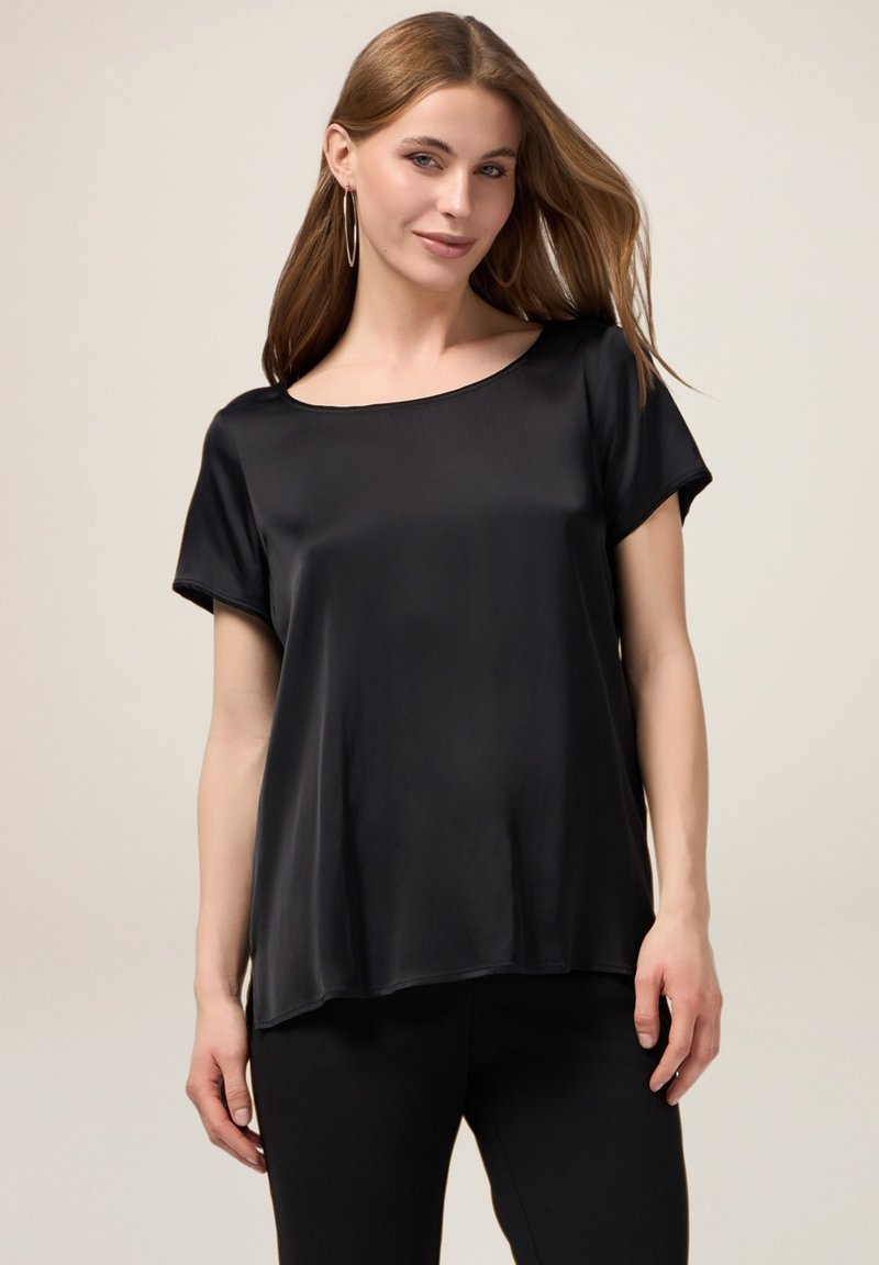 Top corto in satin nero a maniche corte con scollatura ampia e vestibilità morbida. Il tessuto ha una texture liscia, che si drappeggia delicatamente sul corpo.