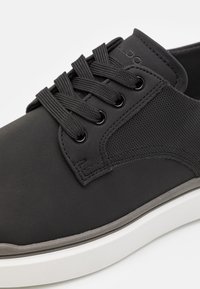 Baskets noires avec une tige lisse mate et des accents en mesh, dotées de lacets ronds, d'un col rembourré et d'une semelle en caoutchouc blanche.