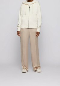 Sudadera cremosa con cremallera y cordones, combinada con pantalones de satén beige claro de pierna ancha y zapatillas blancas. Textura suave y corte relajado.