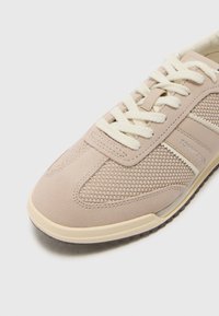 Baskets casual beiges et crème avec textures en mesh et daim, lacets crème, et logo "Tommy Jeans" sur le panneau latéral.