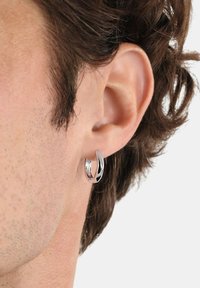 Aro de plata exhibido en la oreja masculina, con un diseño retorcido, superficie pulida y sutiles acentos texturizados.