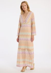 Robe maxi avec un décolleté en V, présentant un motif en zigzag dans des couleurs pastel d'orange, de rose et de vert. Manches longues et détails en texture dentelle.