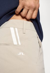 Μπεζ υφασμάτινο παντελόνι με λευκές ρίγες, εφαρμοστή μέση και πλαϊνή τσέπη. Φοριέται κάτω από ναυτικό πουκάμισο, αναδεικνύοντας το υλικό και τις λεπτομέρειες.