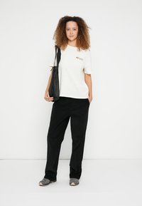 Cream t-shirt with a colorful floral design, black wide-leg pants, and gray sneakers, accessorized with a black tote bag.