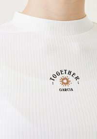 Weißes Rippentop mit hohem Ausschnitt. Auf der Vorderseite befindet sich schwarzer und brauner Text mit den Worten "TOGETHER" und "GARCIA", sowie einer Sonnengrafik.