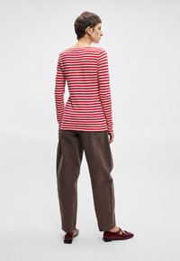 Červený a biely pruhovaný top s dlhým rukávom spárovaný s voľnými hnedými nohavicami. Top má okrúhly výstrih; topánky sú burgundské s detailom pracky.