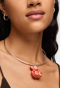 Collana choker con un pendente circolare decorato da motivi concentrici rosa e arancioni. Accompagnata da un semplice collare in metallo argentato.