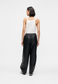 Calças de couro pretas com ajuste descontraído e cintura elástica, combinadas com um top branco sem mangas. O fundo é simples e claro.