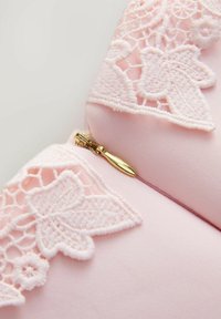 Roosa riie valge lillelise pitsiääre ja väikese kulla tõmblukuga lähedalt vaadatuna.