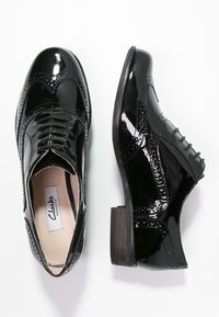 Paire de chaussures brogues en cuir verni noir, une vue de dessus montrant les lacets et l'étiquette de la semelle intérieure, une vue latérale mettant en valeur la semelle et le talon.