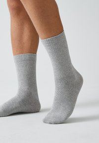 Graue, gerippte Socken aus weichem Material, knöchelhoch mit enganliegendem Sitz, versehen mit einem strukturierten Muster und einem elastischen Bund am oberen Ende.