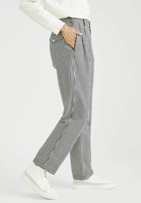 Pantaloni a scacchi bianchi e neri con vita alta, tasche laterali e una vestibilità rilassata, abbinati a scarpe da ginnastica bianche.