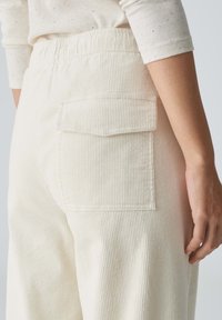 Crème corduroy broeken met verticale ribbels, een achterzak met klep en een elastische tailleband. Soepele textuur en een relaxte pasvorm.