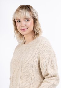 Beige színű, kötött pulóver texturált felülettel, kerek nyakkivágással és hosszú ujjal, fehér háttér előtt bemutatva.