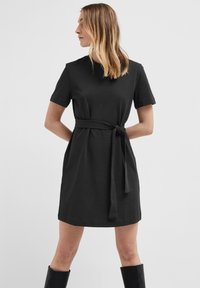 Robe noire à manches courtes fabriquée dans un tissu doux, avec une taille cintrée et une ceinture à nouer, et un design simple à coupe droite.