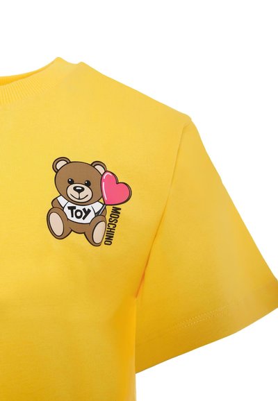 T-shirt en coton jaune avec un graphique d'ours tenant un cœur rose, accompagné du texte "TOY MOSCHINO". Design à manches courtes et col rond.