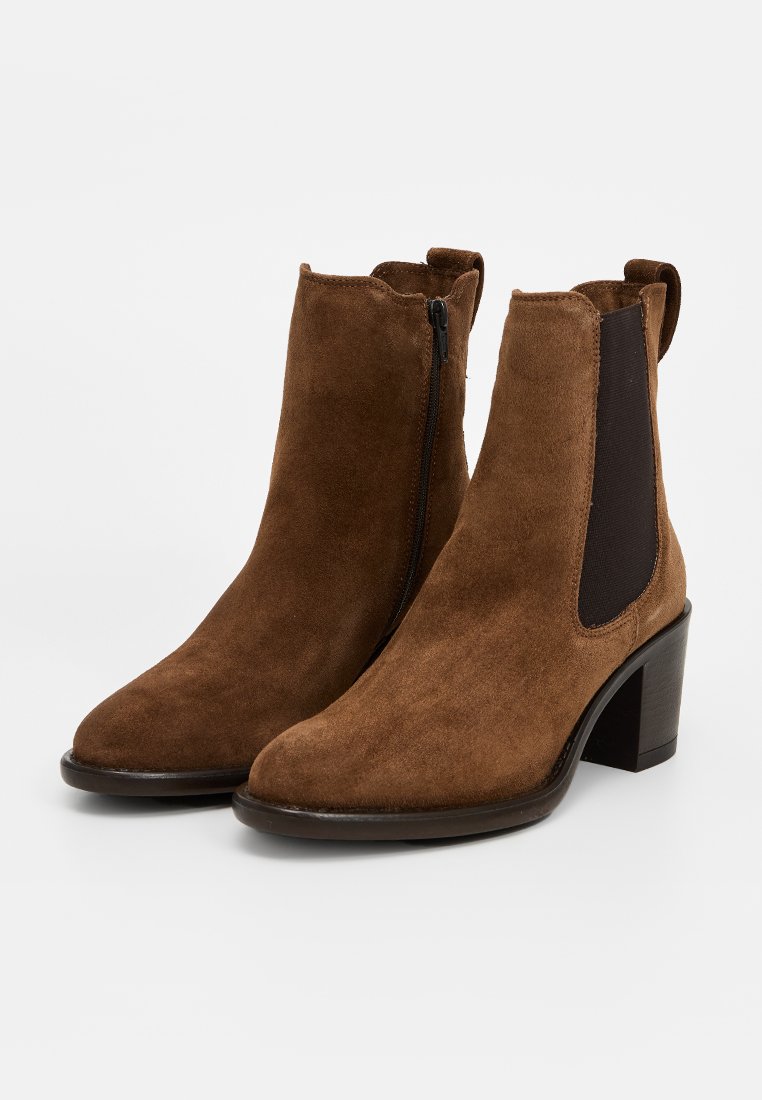 Bottines en daim marron avec un embout arrondi, des panneaux latéraux élastiques et un petit talon bloc. Comprend une fermeture éclair sur le côté et une semelle lisse.