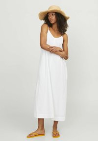 Vestido maxi blanco sin mangas con un corte holgado y tejido texturizado. Combinado con chanclas amarillas y un sombrero de paja de ala ancha.