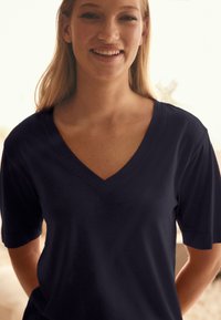 Temno modra majica z V-izrezom in kratkimi rokavi, mehka tkanina, sproščen kroj, z gladko teksturo in nežnim leskom.