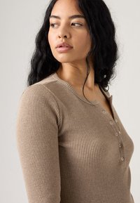 Top de manga larga ribeteado en beige con escote tipo henley, que presenta sutiles botones en el frente y una tela texturizada.