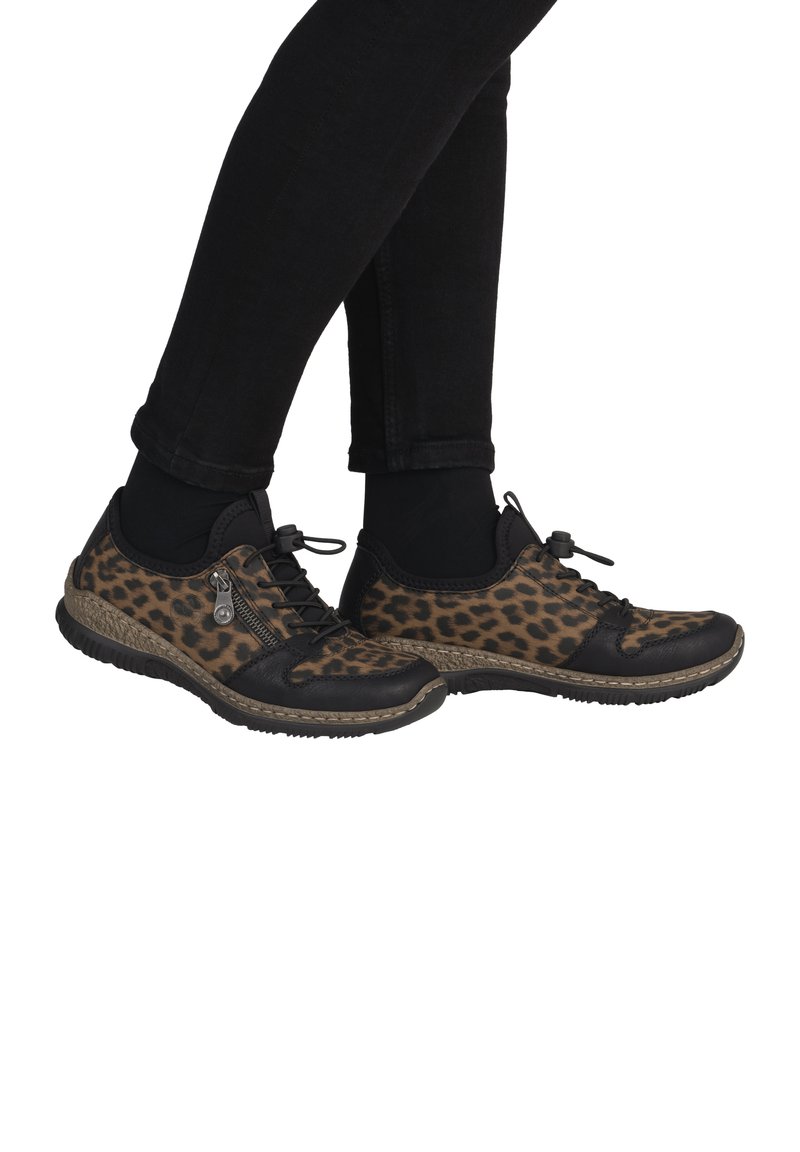 Zapatos de estampado de leopardo con acentos de cuero negro, suela texturizada, diseño con cordones y detalle con cremallera, vistos de lado, combinados con pantalones negros.