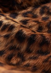 Tissu en fausse fourrure marron présentant un motif léopard avec des taches noires et des textures variées, créant un aspect réaliste de fourrure animale.