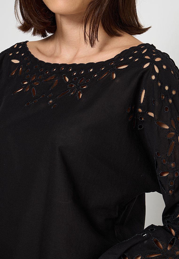 Czarna bluzka z długim rękawem z kwiatowymi wycięciami wzdłuż dekoltu i rękawów, charakteryzująca się gładką, lekką teksturą materiału.