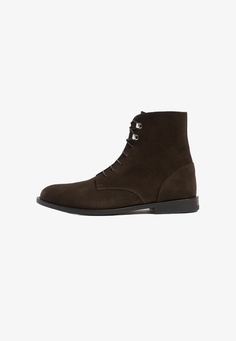 Botas ankle de ante marrón con punta redonda, diseño de cordones, ojales de plata y suela negra lisa. Silueta simple y aerodinámica.