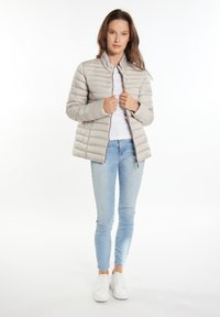 Jachetă pufoasă cu quilted de culoare gri deschis, cu guler înalt, fermoar frontal și un ușor luciu. Purtați peste un top alb și asortată cu blugi deschiși și adidași albi.