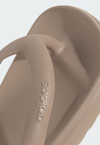 Béžové žabky s textúrovaným gumovým popruhom a stielkou, na popruhu s embosovaným logom "adidas". Jednoduchý a minimalistický dizajn.