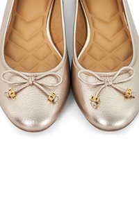 Metallisch beige ballerina's met een textuurleer bovenwerk. Voorzien van een decoratieve strik en kleine gouden accenten bij de teen. Gevoerde binnenzool.