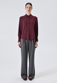 Maroon silk shirt with a classic collar and button front, paired with light grey wide-leg trousers and burgundy shoes. Front view.