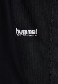 Schwarzer, strukturierter Stoff mit weißem "hummel PERFORMANCE" Logo, gedruckt nahe einer sichtbaren Naht.