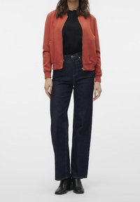 Rode bomberjack met een ritssluiting aan de voorkant, gecombineerd met hoge, donkerdenim rechte jeans en zwarte enkellaarsjes.