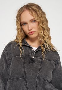 Camicia di denim nera con colletto a bottoni automatici, cuciture visibili e vestibilità rilassata. Presenta una sottile texture e una finitura leggermente usurata.