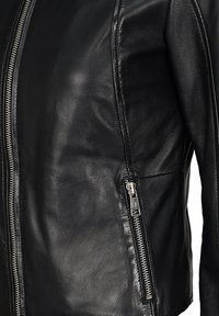 Sort læderjakke med sølvfarvede lynlåse foran og i siden, synlige detaljerede syninger og glat tekstureret materiale.