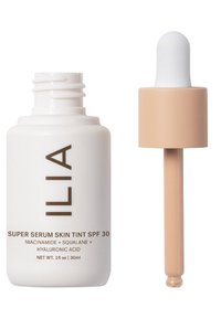 ILIA Super Serum Skin Tint SPF 30 i en vit flaska med brunt text. Har en pipettkork med en ljus beige glödlampa, 30 ml kapacitet.