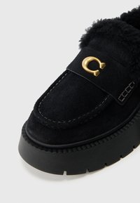 Juodas zomšinis batų tipas loafer su storiu juodu platforminiu padu. Su kailio pamušalu ir auksiniu akcentu ant dirželio. Matomas siuvimo detalė.