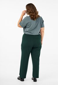 T-shirt grise à manches courtes assortie à un pantalon large vert, fabriqué en tissu doux. Chaussures en laine à enfiler avec une finition lisse.