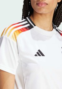 Bílé sportovní tričko s černými akcenty, které má duhové gradientové pruhy na ramenou a texturovaný boční panel. Logo adidas je zobrazeno.