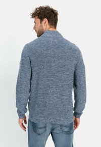 Blauer gestrickter Pullover mit hohem Kragen, strukturiertem Stoff und langen Ärmeln, kombiniert mit Jeans. Die Rückansicht zeigt einen gerippten Saum.